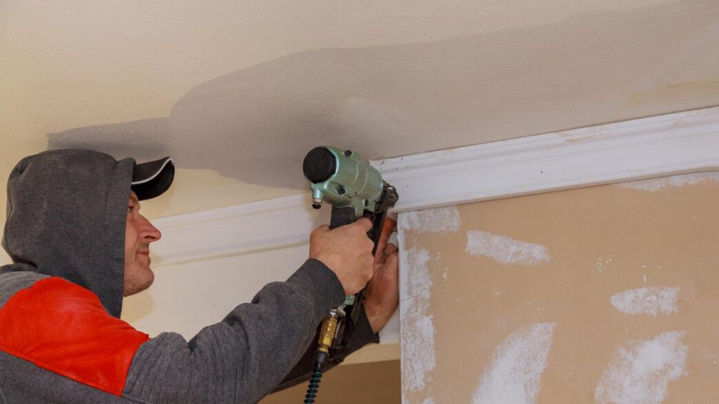 DIY enthusiast installing crown molding in a beautifully decorated living room, surrounded by tools.