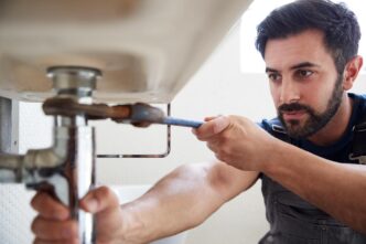 Handyman fixing vintage toilet in a modern bathroom, surrounded by tools and greenery.